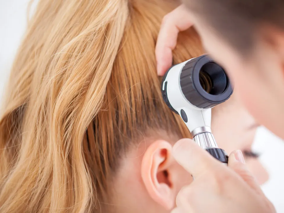 Médica examinando o couro cabeludo de uma paciente com um dermatoscópio